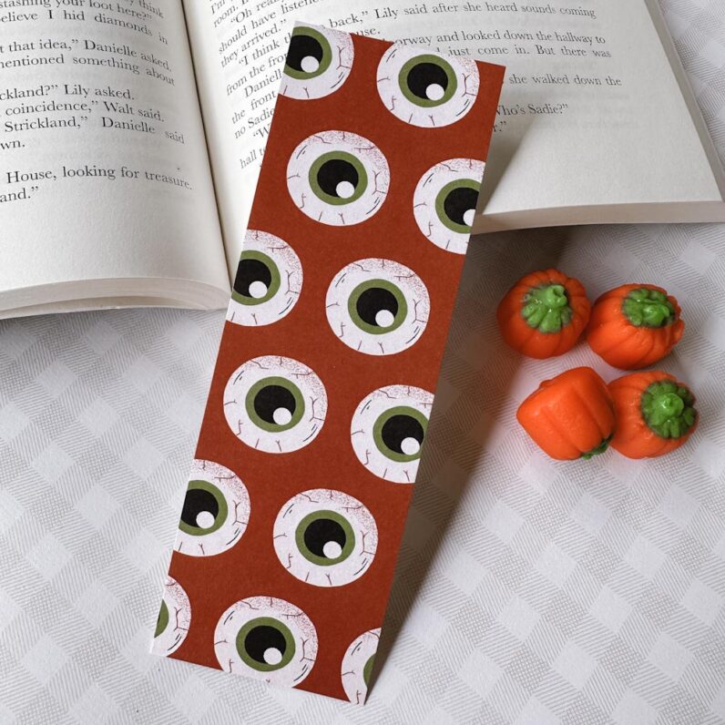 Dark orange bookmark with big round eyeballs with red veins and green-rimmed black pupils.