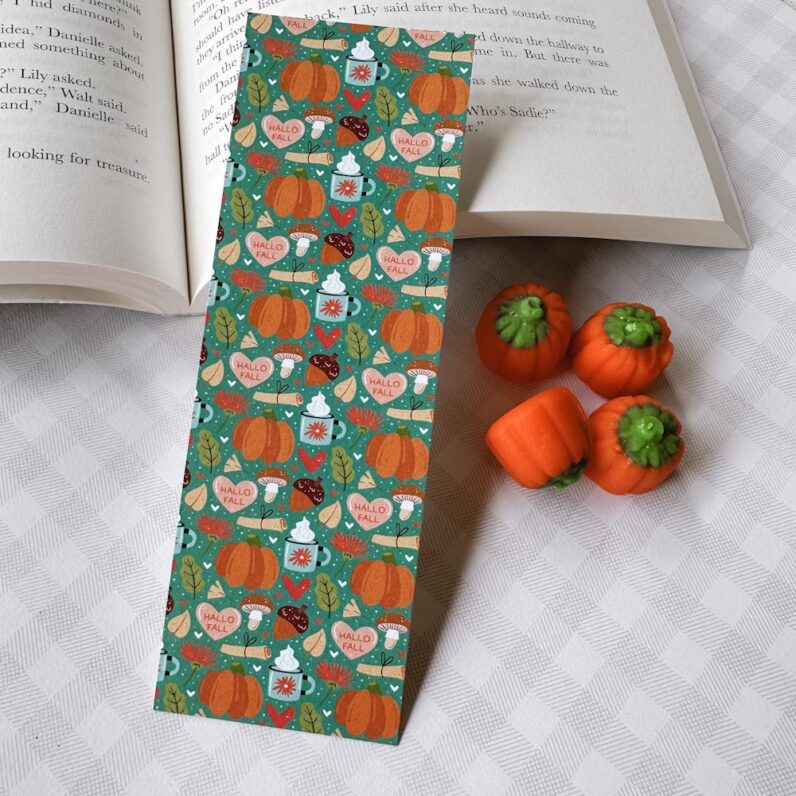 a teal fall themed bookmark covered in fall graphics, like, pumpkins, acorns, leaves, and cups of cocoa.