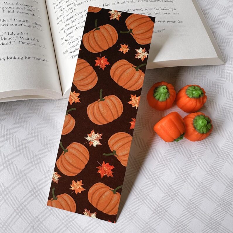 A brown bookmark with orange pumpkins and maple leaves.