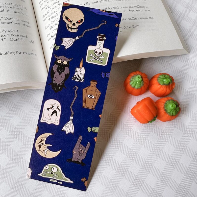 Dark blue bookmark with Halloween images: skulls, broom, owls, candles, skulls, and monsters.